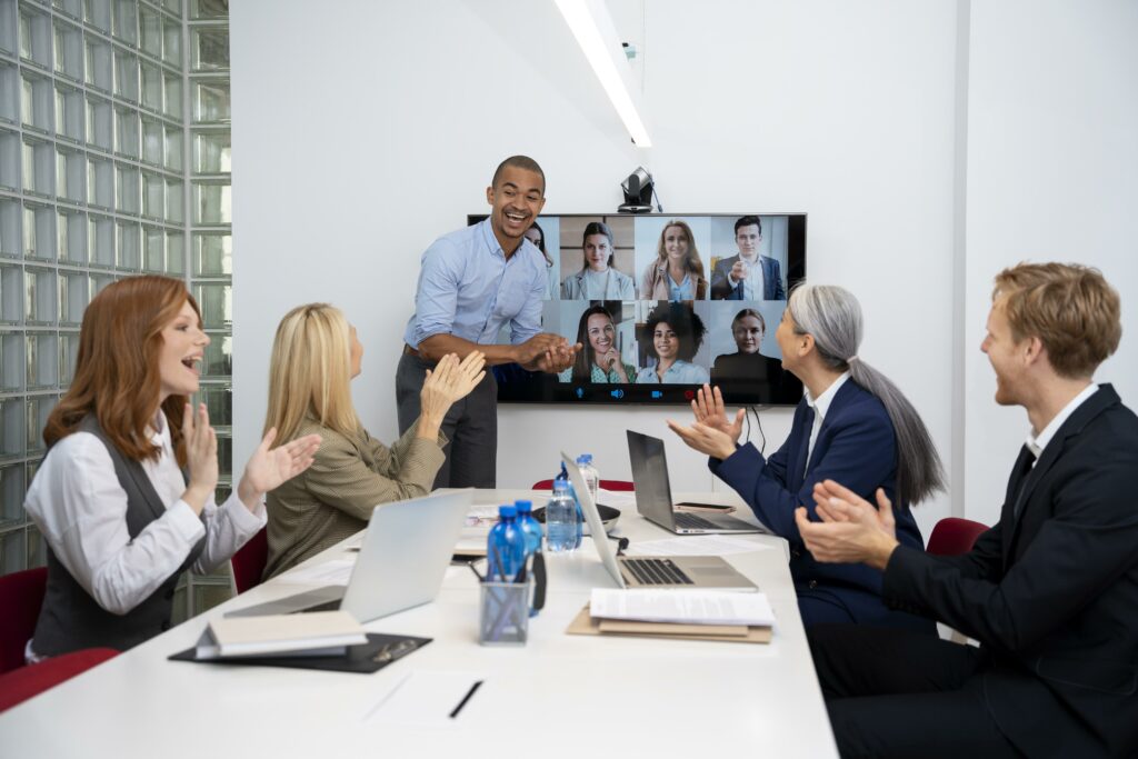 Workers in corporate conference room connect with hybrid workers through virtual conference program.